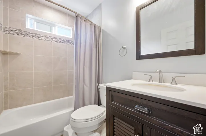 Bathroom featuring a dark wood-finish vanity, undermount sink, brushed nickel faucet, large mirror, and tiled shower surround with an accent mosaic border and high window