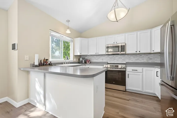 Kitchen featuring white cabinetry, stainless steel appliances, a tile backsplash, wood-finish flooring, and a vaulted ceiling