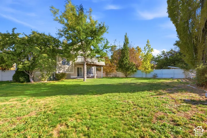 Expansive backyard featuring a large lawn, mature trees, a privacy fence, and a two-story home with a deck and ground-level patio
