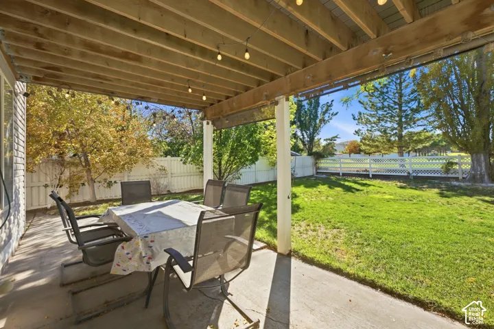 Covered concrete patio with overhead wood joists, a white lattice fence, and a green lawn
