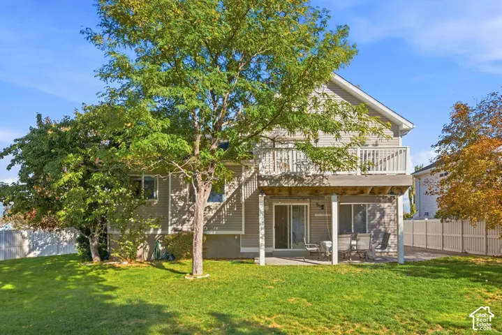 Two-story exterior with horizontal siding, upper-level balcony, ground-level patio, mature trees, and a fenced perimeter