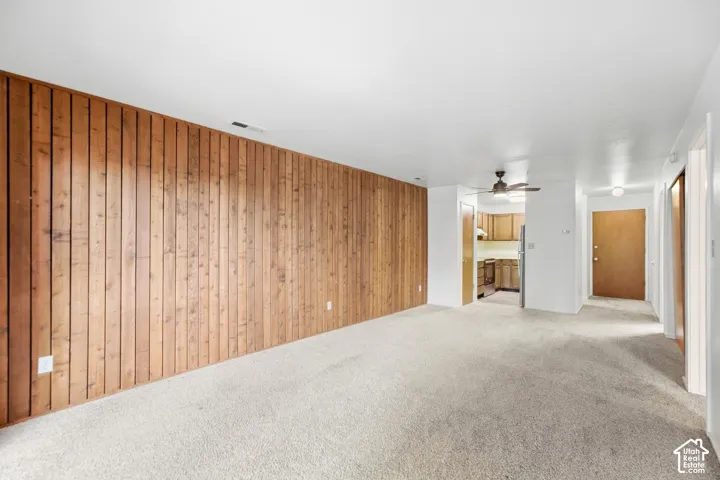 Spacious room with wood paneling, light-colored carpeting, and a ceiling fan