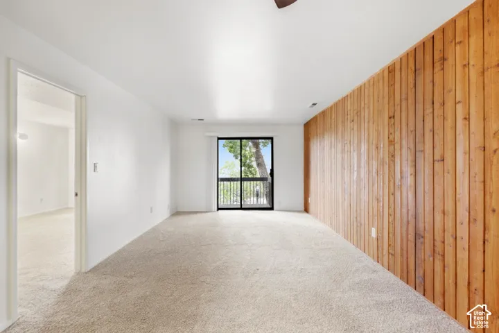 Light-colored carpeted flooring, white painted walls, wood-paneled accent wall, sliding glass door, and ceiling fan