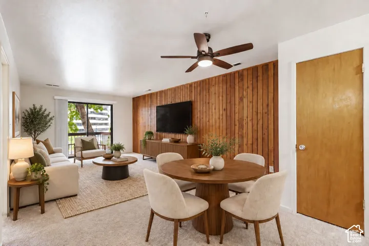 Wood-paneled accent wall, ceiling fan with integrated lighting, wood-finish interior door, and light-colored carpeting