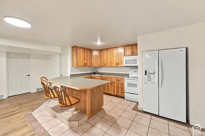 ADU basement - Kitchen featuring wood cabinetry, white appliances, a peninsula with counter seating, and tiled flooring