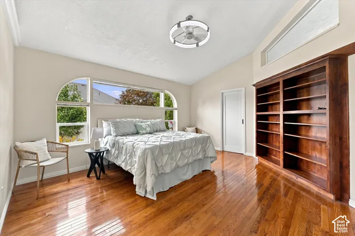 Primary Bedroom - Hardwood flooring, vaulted ceiling, built-in wooden shelving, arched windows, and a modern ceiling fan