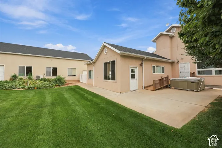 Expansive green lawn, concrete patio, stucco exterior, multiple windows, and exterior entry points