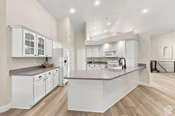 White cabinetry, wood-finish flooring, recessed lighting, vaulted ceiling, and a kitchen island with a built-in sink