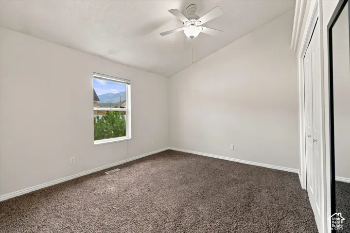 Vaulted ceiling, ceiling fan with integrated lighting, window with mountain backdrop, brown carpet, and white bi-fold closet doors