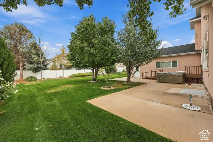 Expansive grassy yard with mature trees, concrete patio, and white privacy fencing