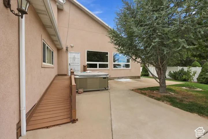 Exterior ramp access to entry door, concrete patio area, and mature landscaping