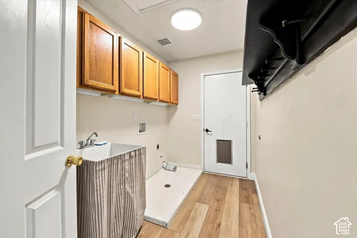 Utility room featuring wood-finish flooring, overhead cabinetry, a utility sink with a chrome faucet, and a built-in wall-mounted coat rack