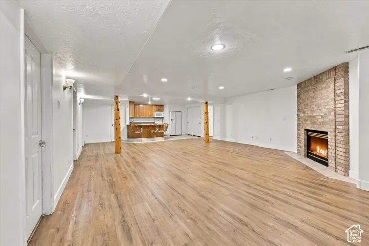 ADU basement - Expansive open-concept room featuring wood-finish flooring, recessed lighting, and a brick-surround fireplace