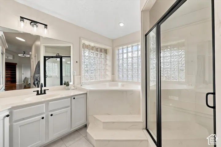 Primary Bathroom - Dual vanity with white cabinetry and matte black fixtures, jetted soaking tub with tile surround, glass block window, and a walk-in shower with black-framed glass enclosure