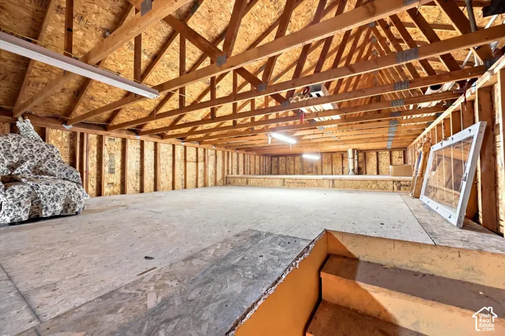 Large Outbuilding. Open attic space with exposed wood trusses and plywood flooring, featuring fluorescent lighting and framed window