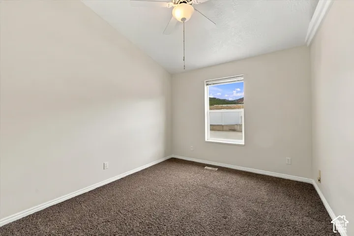 Vaulted ceiling with a flush-mount ceiling fan, neutral wall paint, and a large window