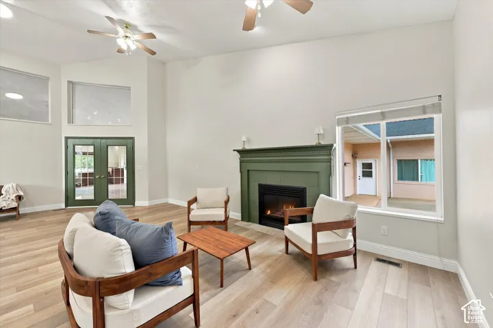 Vaulted ceilings with ceiling fans, wood-finish flooring, a painted fireplace with a mantel, and glass-paned double doors
