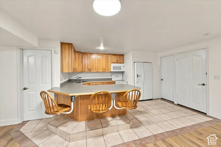 ADU Basement - Kitchenette featuring wood-finish cabinetry, white appliances, and a built-in peninsula with countertop seating