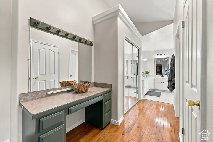 Primary Bathroom - Built-in vanity with countertop and mirror, wood-finish flooring, vaulted ceiling, and mirrored closet doors