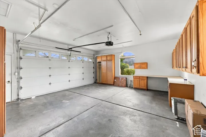 Spacious garage featuring a finished concrete floor, built-in wooden cabinetry, an arched window, and a workbench surface