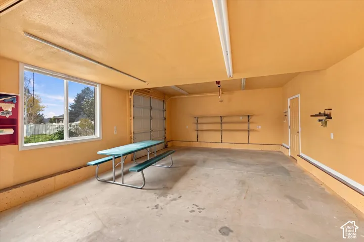 Large Outbuilding. Attached garage featuring concrete flooring, fluorescent overhead lighting, an exterior window, and built-in shelving