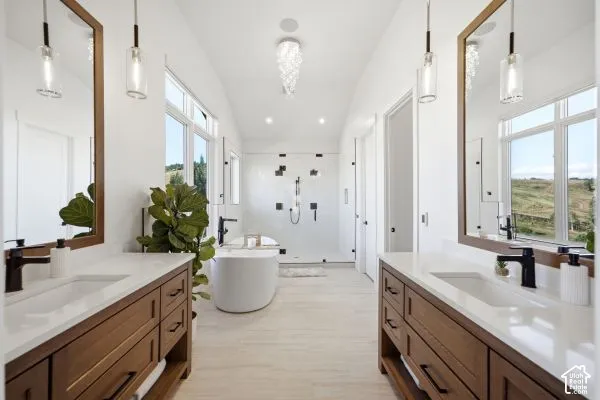Dual wood-finish vanities with undermount sinks, a freestanding soaking tub, a spacious glass-enclosed shower, and a crystal chandelier