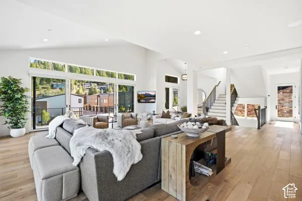 Vaulted ceilings, expansive glass sliding doors, wood-finish flooring, recessed lighting, and a modern staircase with dark wood railings