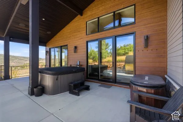 Covered patio featuring a hot tub, concrete flooring, exterior wood siding, and large sliding glass doors