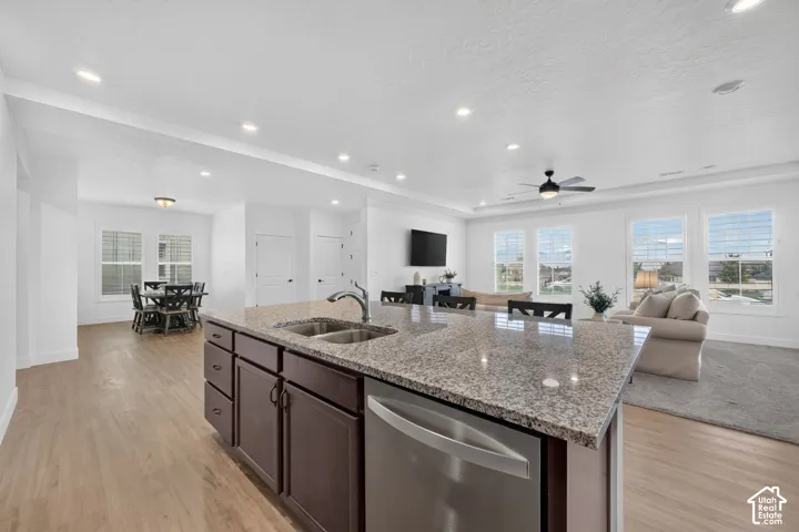 Kitchen island with a stone countertop and integrated stainless steel sink, wood-finish flooring, recessed lighting, and multiple windows