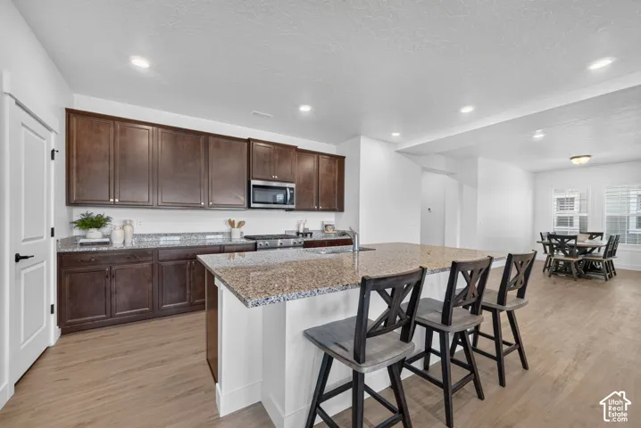 Kitchen featuring dark wood-finish cabinetry, light speckled countertops, a stainless steel microwave, and wood-finish flooring
