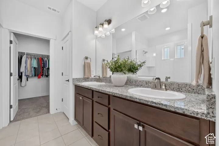 Bathroom featuring a dual-sink vanity with granite countertops, wood-finish cabinetry, and a framed mirror
