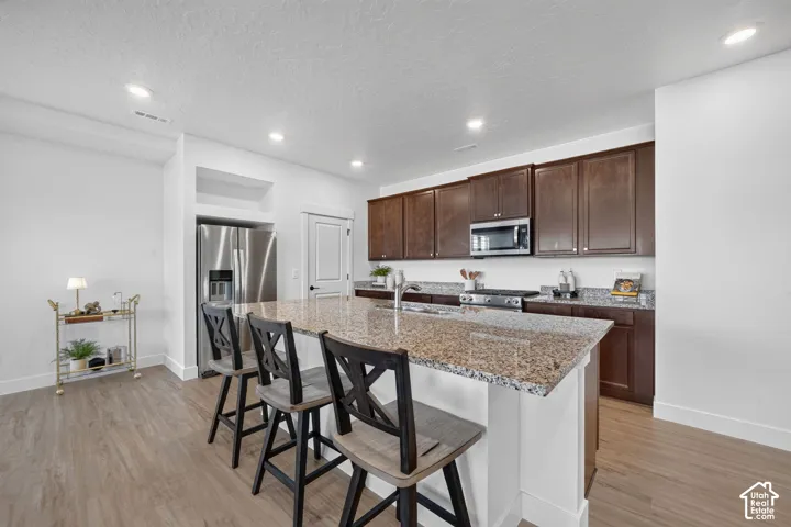 Kitchen featuring a large island with stone countertop, stainless steel appliances, dark wood cabinetry, and wood-finish flooring