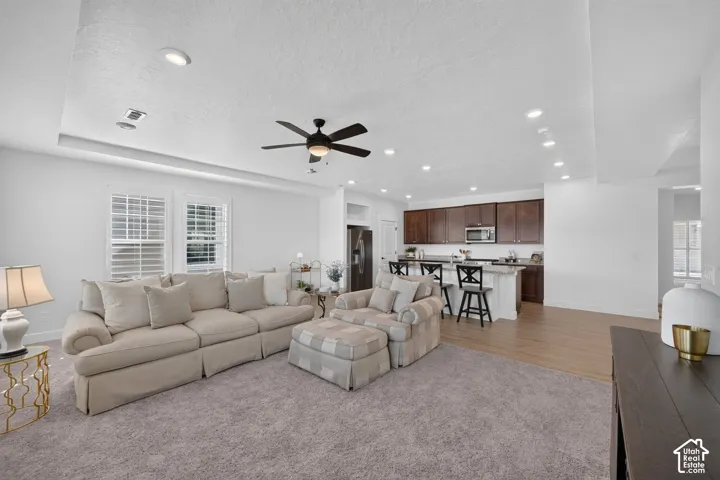 Tray ceiling with recessed lighting, ceiling fan, plantation shutters, wood-finish flooring, and dark wood cabinetry