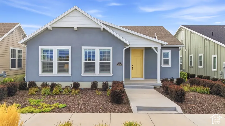 Stucco exterior with contrasting trim, covered entry, yellow front door, multiple windows with blinds, and established landscaping
