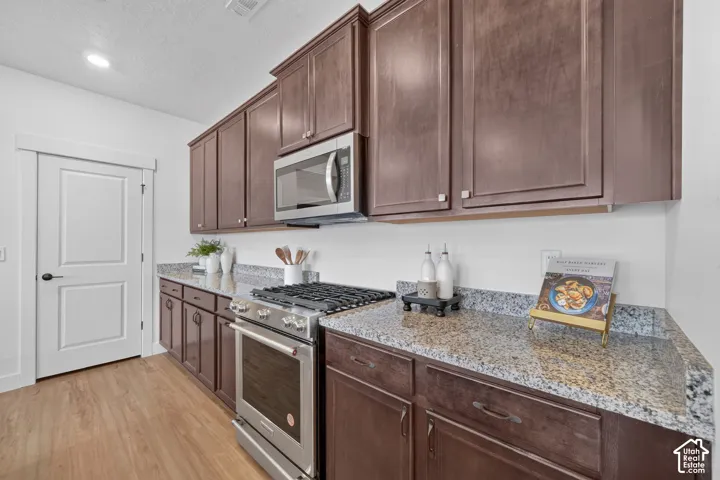 Extensive upper and lower cabinetry, stainless steel oven with gas cooktop, built-in microwave, wood-finish flooring, and speckled countertops