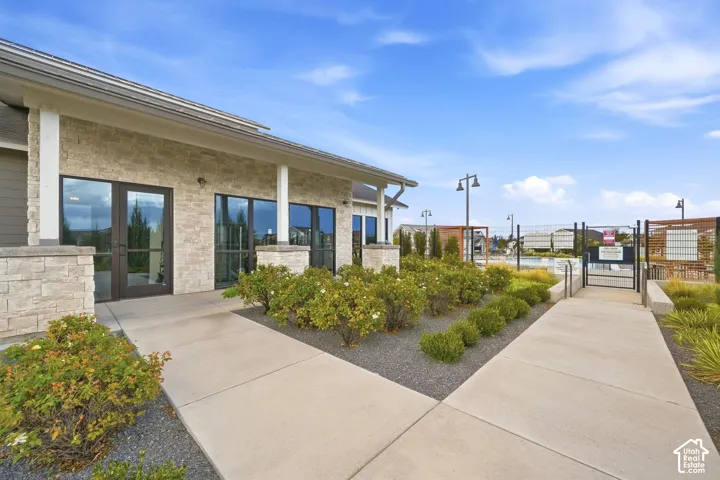 Stone veneer facade with multiple glass entry doors, concrete pathways, and cultivated landscaping