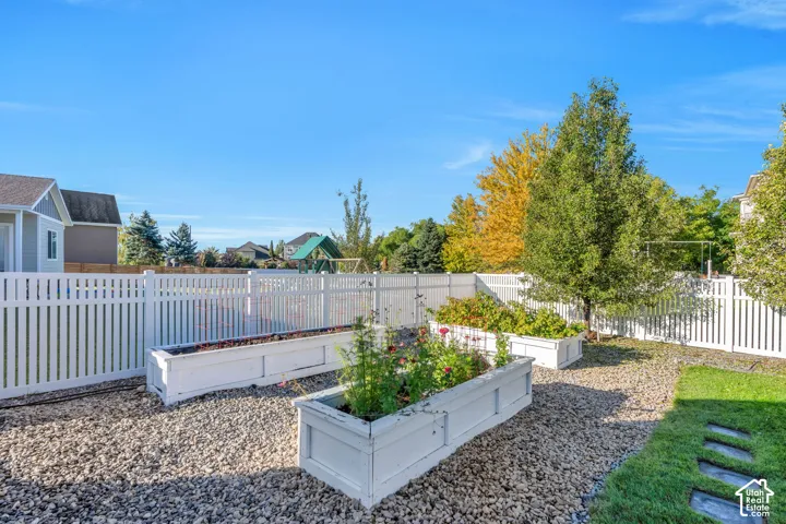 Backyard featuring a white picket fence, gravel landscaping, raised garden beds, and mature trees