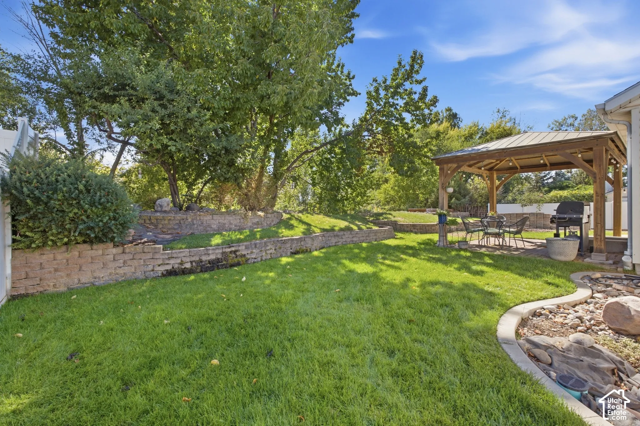 Manicured lawn with a decorative rock border, retaining walls, and a wooden gazebo with a metal roof