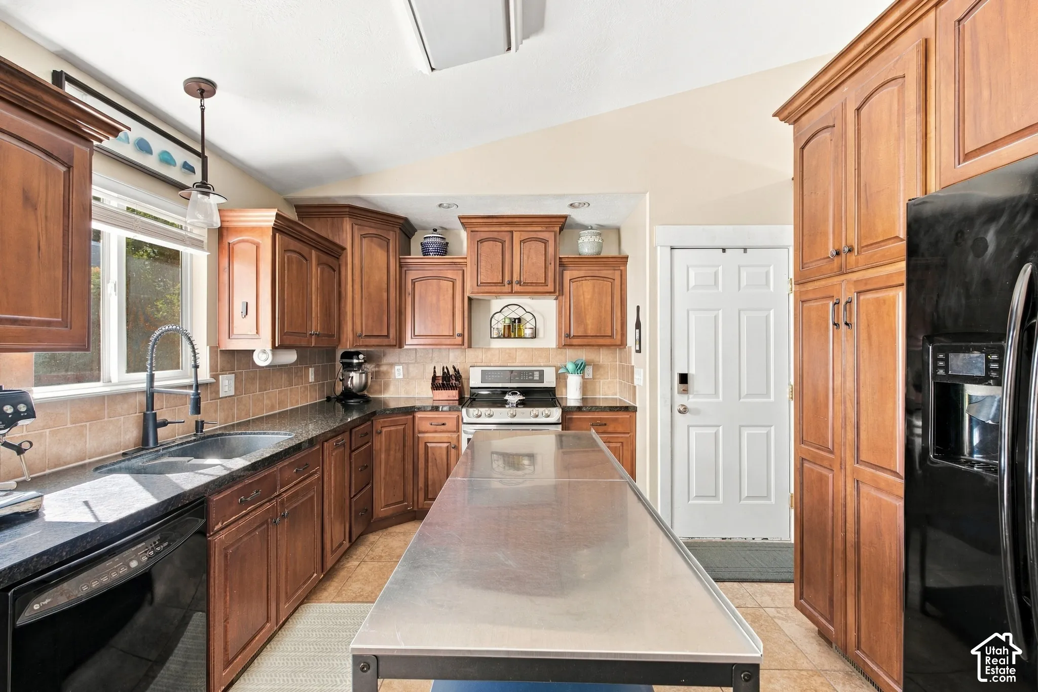 Kitchen featuring wood cabinetry, black countertops, a stainless steel sink with a high-arc faucet, and tile flooring