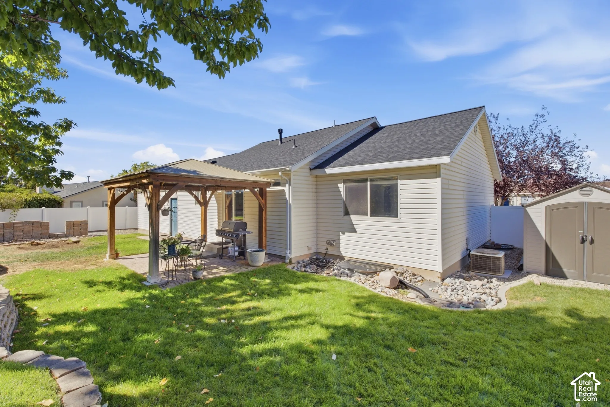 Expansive backyard featuring a manicured lawn, a paved patio with a built-in wooden gazebo, and a storage shed