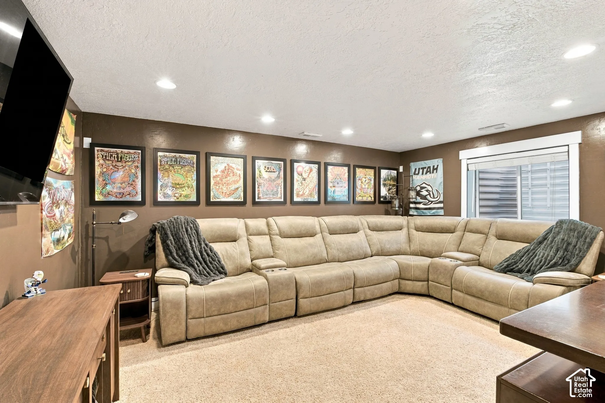Recessed ceiling lighting, a mounted television, a large window with blinds, and carpeted flooring