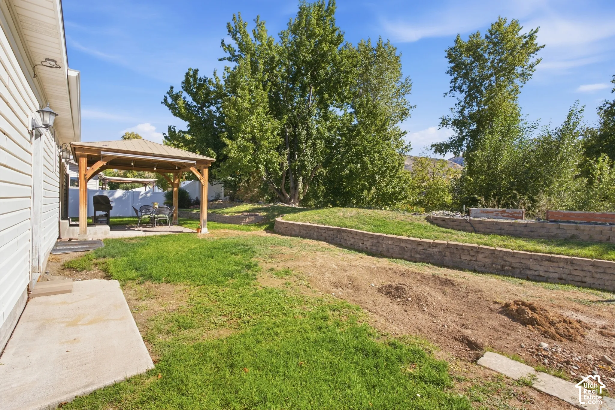 Patio with a pergola, concrete hardscaping, and tiered landscaping with stone retaining walls
