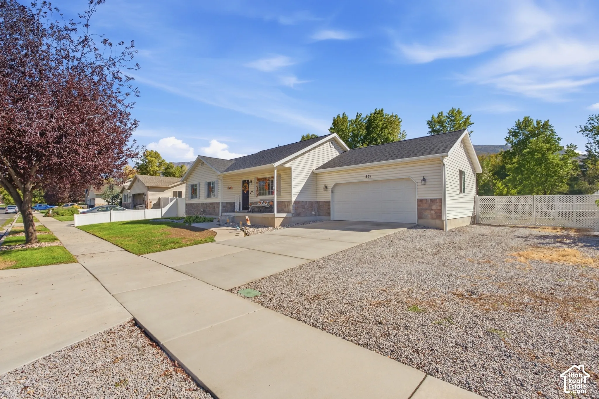 Single-story residence featuring light-colored siding, a covered front porch, an attached garage, a paved driveway, and a gravel yard
