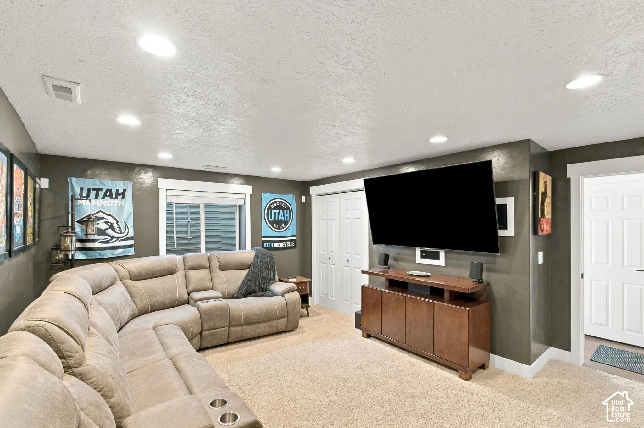 Recessed lighting, wood-finish media console, built-in shelving, carpeted flooring, and a white paneled door