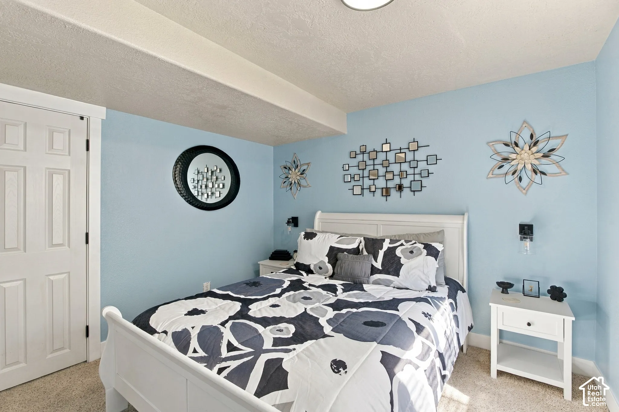 Wall-mounted lighting fixtures, soft blue wall finish, white paneled door, and carpeted flooring