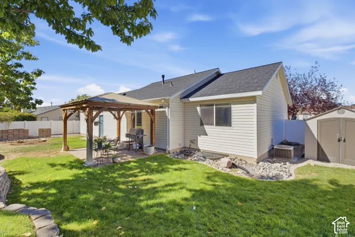 Expansive backyard featuring a manicured lawn, a paved patio with a built-in wooden gazebo, and a storage shed