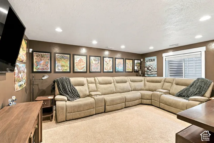 Recessed ceiling lighting, a mounted television, a large window with blinds, and carpeted flooring