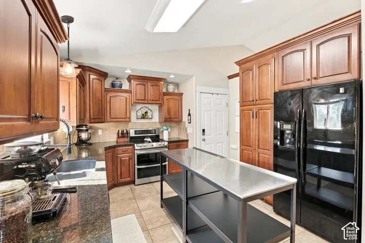 Kitchen featuring wood cabinetry, dark countertops, stainless steel appliances, and tile flooring