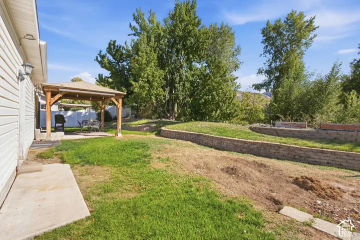 Patio with a pergola, concrete hardscaping, and tiered landscaping with stone retaining walls
