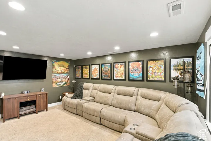 Recessed ceiling lighting, wall-mounted television, wood-finish media console, neutral-toned carpeting, and painted walls